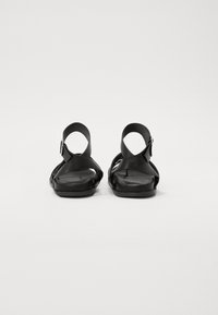 Black sandals with cross-strap design, flat sole, and ankle buckle. Made of smooth material, featuring a minimalistic shape.