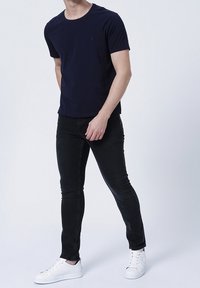 Námořnicky modré tričko s krátkým rukávem a kulatým výstřihem, doplněné úzkými černými džíny a bílými teniskami, s minimalistickým designem.