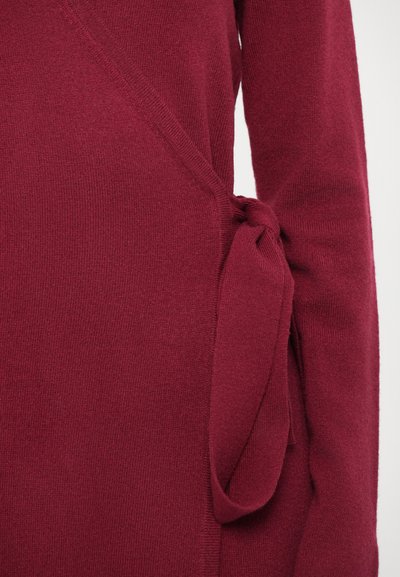 Burgundy knit wrap top featuring a side tie detail. The texture is soft, with a smooth finish and a fitted silhouette.