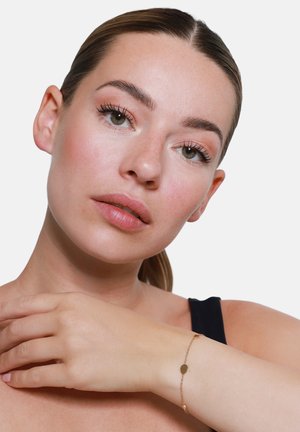 Bracelet en ton or avec de petits maillons ovales et ronds, élégamment fixé sur un poignet à la peau lisse et brune.