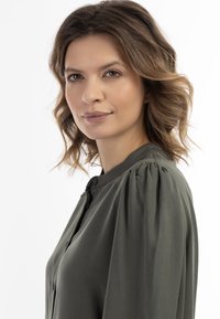 Olijfgroene blouse met een knoopsluiting aan de voorkant,Gathered puffmouwen en een zachte stoftextuur. Minimalistisch ontwerp en klassiek kraagdetail.