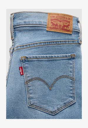 Lyseblå denimjeans med en mærket læderlap, en rød mærkat på baglommen og karakteristisk syning i et buet mønster.