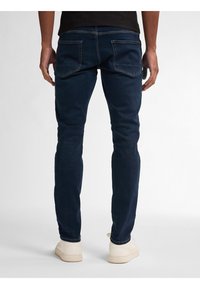 Tmavě modré džíny s úzkým střihem, se zadními kapsami a jemnými švy. V kombinaci s světle barevnými teniskami.