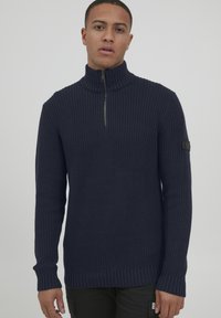 Maglione lavorato a maglia blu navy con collo alto, mezza zip, polsini e orlo a coste. Include un motivo testurizzato e una etichetta con logo sulla manica.