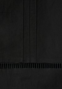 Tissu noir avec des coutures verticales et une bande découpée horizontale présentant des ouvertures rectangulaires régulièrement espacées.