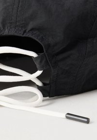 Fekete szövet táska fehér zsinórokkal, sima textúrával és hengeres alakú, kiemelve a varrási részleteket és egy fekete csúszkát.