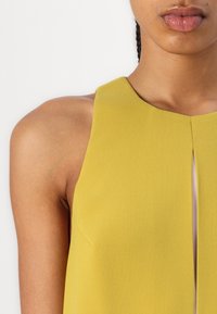 Sleeveless yellow top with a rounded neckline and a vertical slit at the center. Made of a soft, textured fabric.