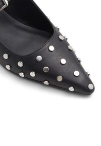 Chaussure en cuir noir à bout pointu avec des clous ronds argentés et une bride à boucle.
