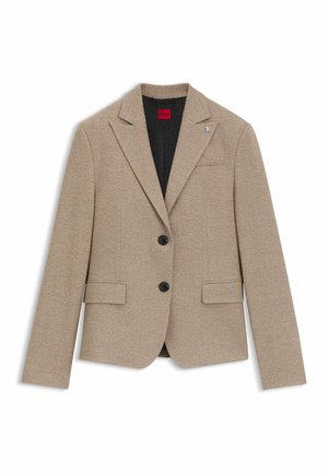 Blazer beige con due bottoni neri, revers a punta, due tasche frontali e una texture sottile; presenta un distintivo con il marchio sul revers sinistro.