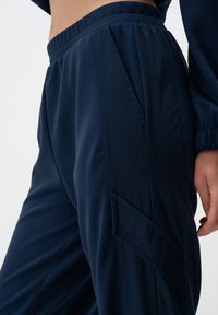 Pantalons de sport bleu marine avec une texture lisse, dotés d'une poche cargo sur le côté et d'une taille froncée pour un maintien sûr.