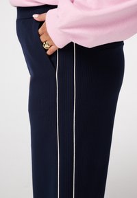 Marineblauwe ribbroek met een rechte pijp, voorzien van een witte zijstreep en een zak. Gecombineerd met een lichtroze trui.