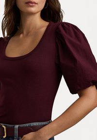 Burgunderfärgad ribbad bodysuit med korta puffärmar. Den har en rundad halsringning och är i kombination med en denimmidja och bälte.