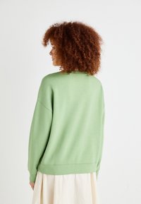 Světle zelená mikina s volným střihem, spadlé ramena a žebrované manžety. Měkká textura, minimalistický design, bez viditelných vzorů nebo ozdob.