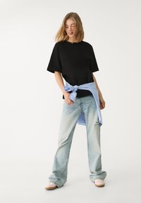 Sort oversized t-shirt parret med lyseblå, slidte wide-leg jeans. En lyseblå stribet skjorte bundet om livet tilføjer kontrast.