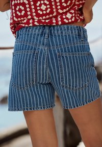 Shorts en denim rayés bleu et bleu clair, dotés de poches arrière, d'une taille haute et d'un ourlet surpiqué. Le tissu a une texture lisse.