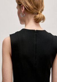 Zwart mouwloos jurk met een hoge halslijn en een verborgen rits aan de achterkant. Glad, gestructureerd textiel met subtiele naden.
