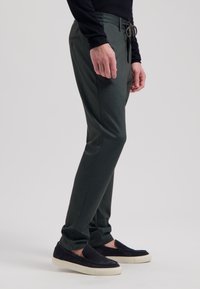 Mørkegrønne bukser lavet af blødt stof, med snoretræk i taljen, slim fit og to sidelommer. Kombinationen med sorte slip-on sko.