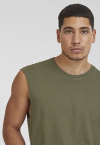 Maglietta senza maniche verde oliva in tessuto morbido, con scollatura rotonda e dettagli di cucitura puliti, che mette in mostra un design dal taglio rilassato.