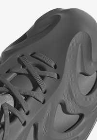 Grijze sneaker van textuur rubbermateriaal, met een uniek golfontwerp, prominente uitsparingen en platte veters.