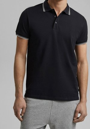 Polo shirt nera in cotone, con colletto a tre bottoni, rifiniture bianche a contrasto su colletto e maniche, e una vestibilità rilassata.