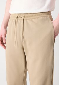 Beige joggebukser laget av mykt stoff, med elastisk midjebånd og snor, sidelommer og en avslappet passform.