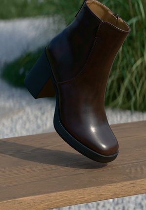 Dark brown leather ankle boot with block heel resting on wooden surface outdoors with blurred grass background.