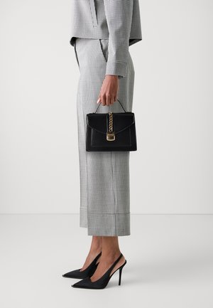 Czarna torebka z łańcuszkowym detalem, o uporządkowanym kształcie i złotych elementach, zestawiona z kraciastym garniturem i czarnymi szpilkami.