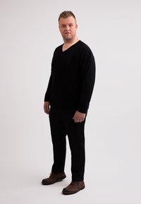 Svart V-ringad tröja och svarta byxor, kombinerat med bruna snörskor. Outfiten har en enkel design och en figursydd silhuett.