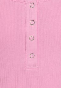 Rosa ribbat tyg med en knappslå som har fem metalliska silveröglor. Slät textur, figurnära design med rundad halsringning.