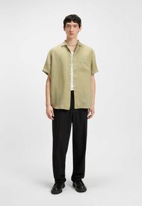 Korte mouwen, licht olijfkleurig linnen shirt met een borstzak, gecombineerd met zwarte broek en chunky zwarte schoenen. Netjes gekraagd, relaxte pasvorm.