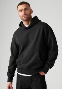 Sudadera con capucha negra hecha de tejido suave, con un bolsillo canguro y puños de canalé. Detalle sutil del logotipo en la parte delantera.