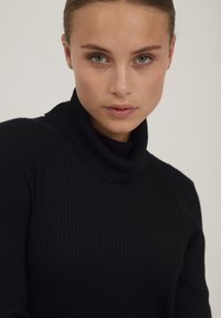 Maglione nero a collo alto con design aderente e tessuto testurizzato, caratterizzato da un collo alto e maniche lunghe.