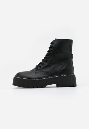 Black leather lace-up combat boot with thick lug sole and white stitching detail, viewed from the side on a white background.
