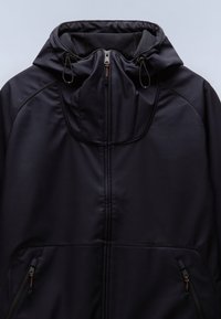 Veste noire à capuche avec fermeture éclair frontale, cordons réglables sur la capuche et poches zippées des deux côtés.