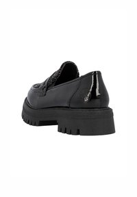 Mocassins en cuir verni noir avec une tige en tissu texturé, semelles en caoutchouc épaisses et détail de logo embossé sur le côté.