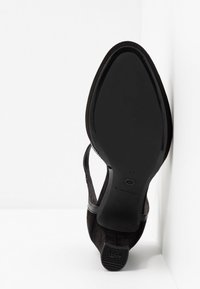 Chaussure de ville noire pour femme avec bout pointu et semelle antidérapante, vue par le dessous sur fond blanc.