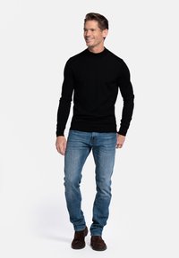 Zwarte trui met lange mouwen en ronde hals, gecombineerd met lichtblauwe jeans en donkerbruine suède laarzen. Eenvoudig ontwerp, aangesloten silhouet.