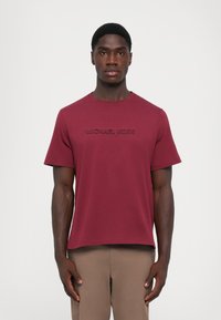 Mørkerød bomulds T-shirt med korte ærmer og rund halsudskæring med et præget "MICHAEL KORS" logo over brystet.