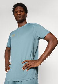 T-shirt de sport bleu clair en tissu évacuant l'humidité. Présente un col rond, des manches courtes et des accents de logo orange sur la poitrine.