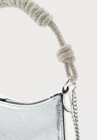 Bolsa de mão metálica prateada com superfície texturizada, apresentando uma alça de corrente com nó e fecho de zíper. Contém detalhes em metal prateado.