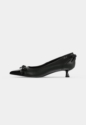 Chaussure pour femme en cuir noir, à talon bas, bout pointu, avec un petit nœud décoratif à l’avant et un talon légèrement évasé.