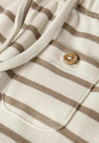 Gestreepte katoenen stof in beige en bruin, met een kleine borstzak met een houten knoop en een gladde stiksels langs de randen.