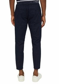 Granatowe spodnie o prostym kroju, z elastycznym pasem, dwoma tylnymi kieszeniami, zestawione z białymi sneakerami. Gładka faktura materiału.