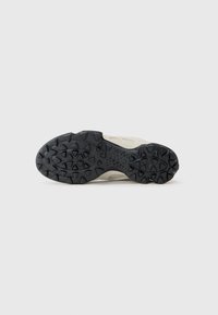 Schwarze Gummi-Außensohle mit strukturiertem Grip-Muster; hellfarbiger Oberteil mit glatter Oberfläche und minimalen Designdetails.
