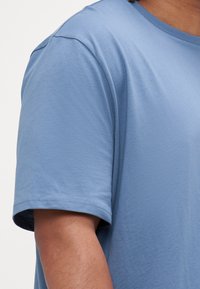 T-shirt en coton bleu clair avec un col rond et des manches courtes. Présente une texture lisse et des ourlets proprement cousus sans embellissements.