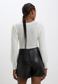 Maglione bianco lavorato a maglia con maniche a sbuffo lunghe, abbinato a pantaloni corti in pelle nera a vita alta con dettaglio della zip sul retro.