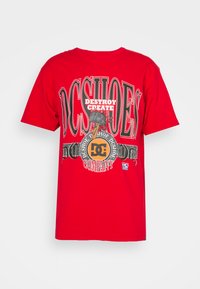 T-shirt en coton rouge avec un grand imprimé graphique en noir et blanc avec le texte "DC SHOES" et "DESTROY CREATE", col rond et manches courtes.