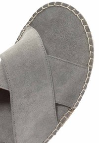 Sandalo grigio in suede con cinturini incrociati e superficie testurizzata. Presenta una suola beige intrecciata con un bordo cucito per un ulteriore dettaglio.