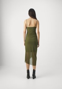 Grön, figursydd slipklänning med tunna axelband, genomskinlig nederdel, längd till mitten av vadbenet, kombinerad med svarta klackade ankelstövlar.