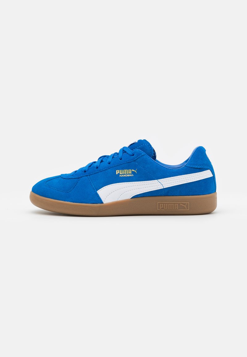 Blauwe suède sneakers met witte accenten en gouden branding. Heeft ronde veters en een gumrubberen zool. Zijaanzicht, platte vorm.